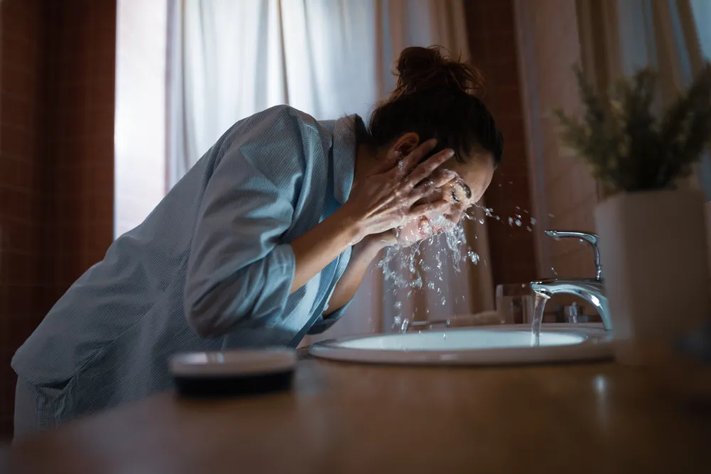 Junge Frau wäscht sich im Badezimmer das Gesicht mit Wasser